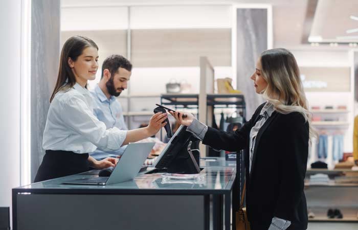 Young woman at clothing store paying for goods with retail assistant.