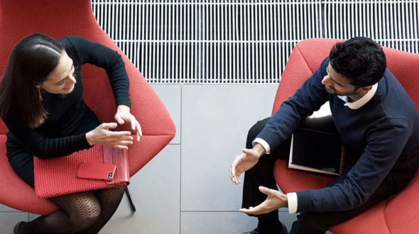 business man and business woman discussing together in a meeting, sitting on red chairs, viewed from above.